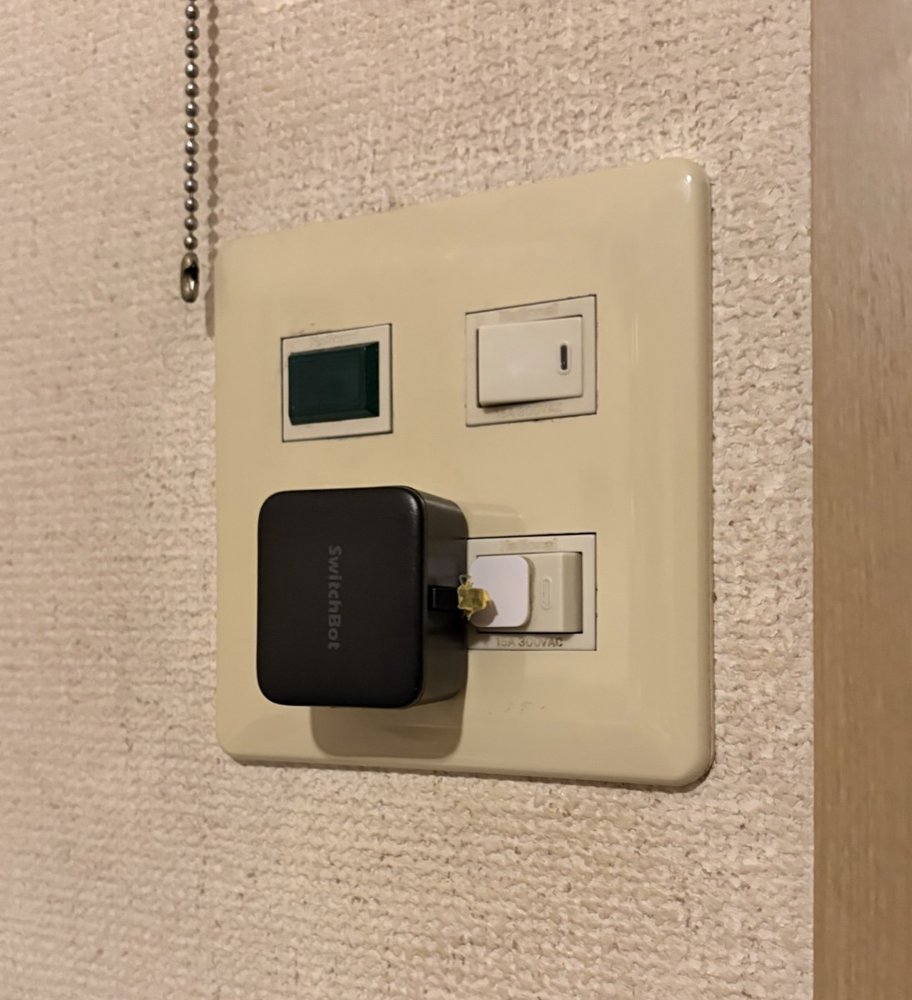 玄関の壁スイッチに両面テープで取り付けた黒いSwitchBotスイッチ