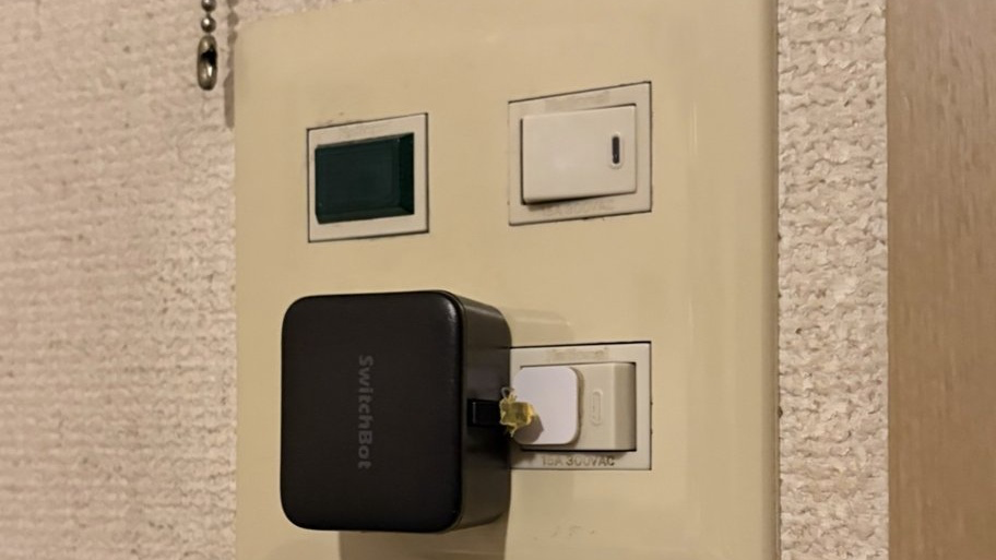 玄関の壁スイッチに両面テープで取り付けた黒いSwitchBotスイッチ